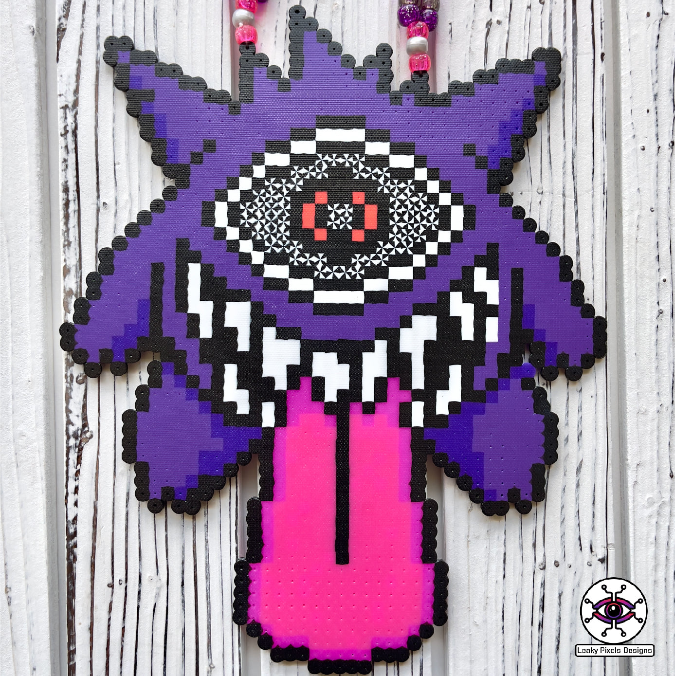 Gengar Subtronics Perler Necklace. Purple ghost pokemon that has a hypnotizing cyclops eye, sharp looking teeth and long pink tongue sticking out.