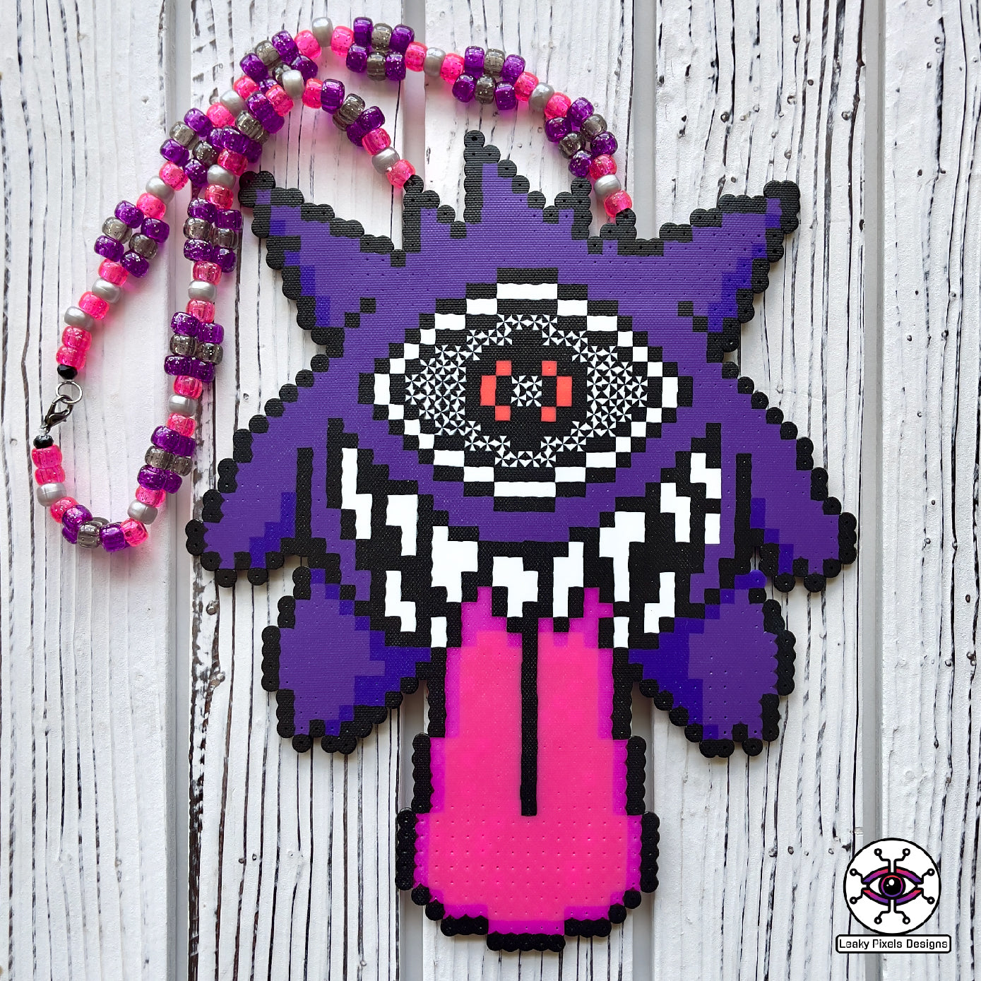 Gengar Subtronics Perler Necklace. Purple ghost pokemon that has a hypnotizing cyclops eye, sharp looking teeth and long pink tongue sticking out.