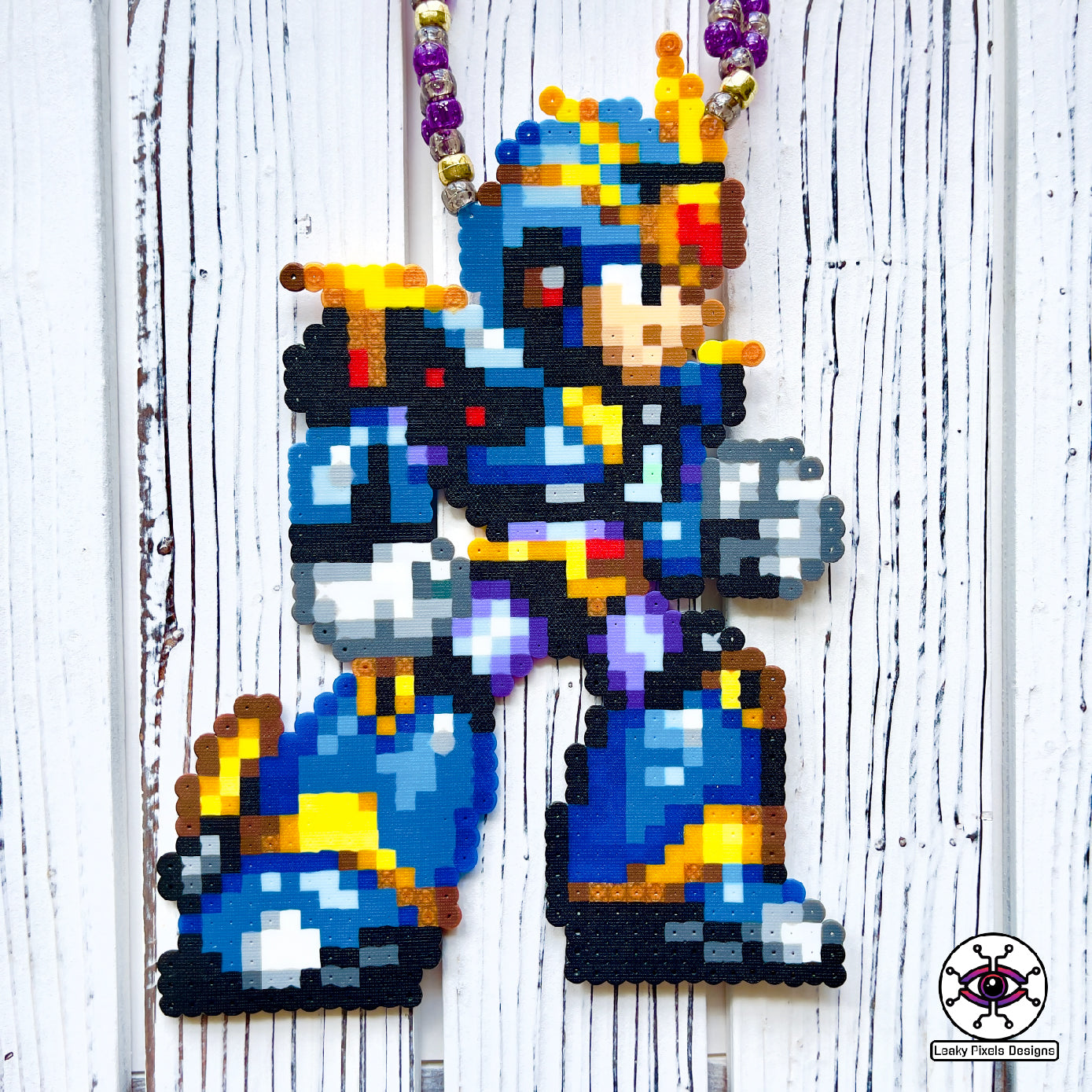 Megaman X Ultimate Armor perler necklace made by Leaky Pixels. Blue, black and gold armor of megaman facing right. Necklace is made with purple and black glitter beads and also gold beads.