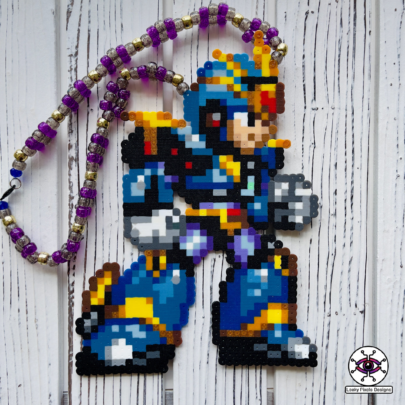 Megaman X Ultimate Armor perler necklace made by Leaky Pixels. Blue, black and gold armor of megaman facing right. Necklace is made with purple and black glitter beads and also gold beads.