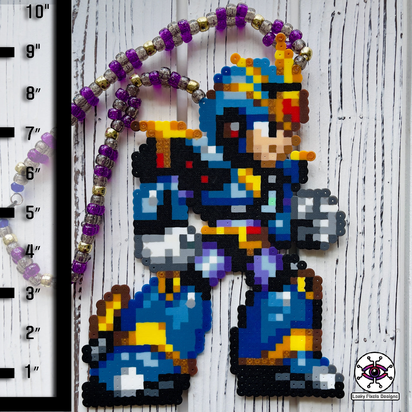 Megaman X Ultimate Armor perler necklace made by Leaky Pixels. Blue, black and gold armor of megaman facing right. Necklace is made with purple and black glitter beads and also gold beads.