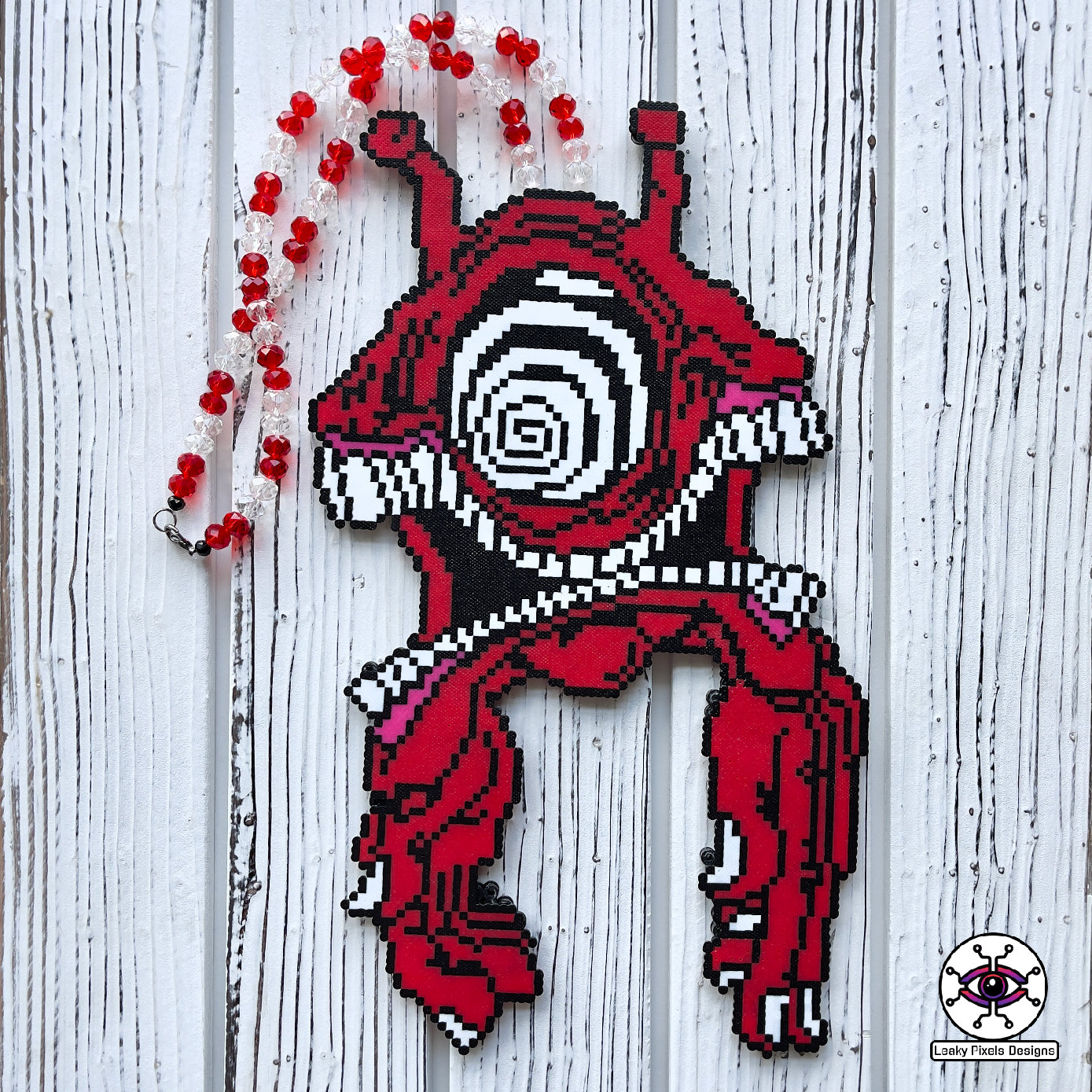 Subtronics cyclops red perler necklace made by leaky pixels. Red cyclops with hypnotizing swirl eye. three mouths all connected together with two large hands connected to it and two antennas. Red glitter and silver pony beads