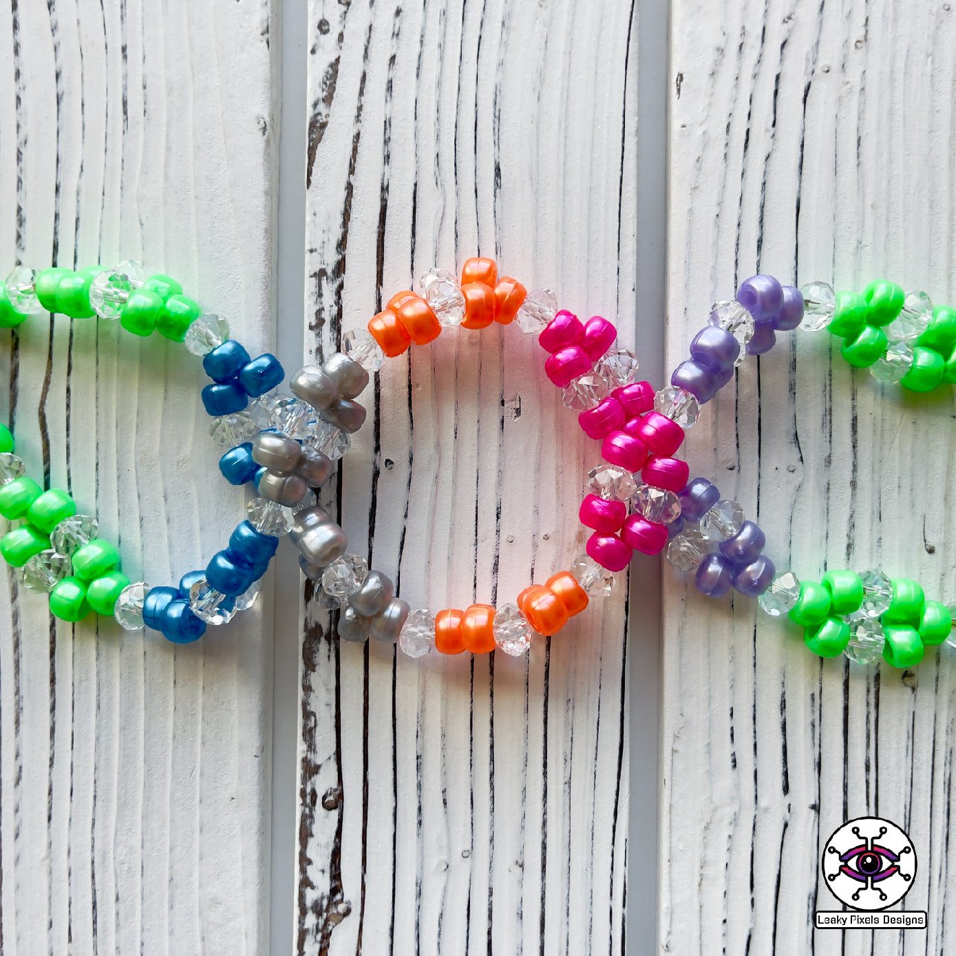 hyper sonic perler necklace by leaky pixels. yellow hyper sonic with stars around him, placed over 7 super emeralds green, blue, light blue, white, pink, orange and purple, on top of a gold ring. necklace is made of same colors of gems.