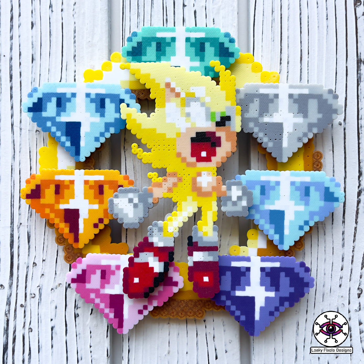 hyper sonic perler necklace by leaky pixels. yellow hyper sonic with stars around him, placed over 7 super emeralds green, blue, light blue, white, pink, orange and purple, on top of a gold ring. necklace is made of same colors of gems.